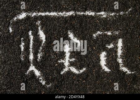 Kalligraphische Inschrift gotischen Buchstaben Kaffee über trockenes schwarzer Ceylon Tee verstreut auf weißem Marmor. Kaffee trinken Konzept Hintergrund. Ansicht von oben Stockfoto