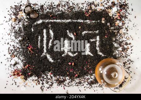 Kalligraphische Inschrift gotischen Buchstaben Kaffee über trockenes schwarz Ceylon und grüner Tee verstreut auf weißem Marmor mit Rosenknospen, stainer, Teekanne aus Glas. Tee d Stockfoto