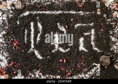 Kalligraphische Inschrift gotischen Buchstaben Kaffee über trockenes schwarz Ceylon und grüner Tee verstreut auf weißem Marmor mit Rosenknospen und stainer. Kaffee trinken con Stockfoto