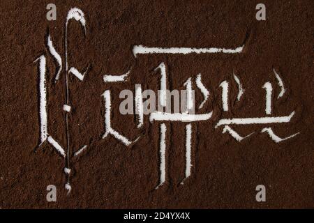 Kalligraphische Inschrift gotischen Buchstaben Kaffee über Grund schwarzer Kaffee verstreut auf weißem Marmor. Kaffee trinken Konzept Hintergrund. Ansicht von oben Stockfoto