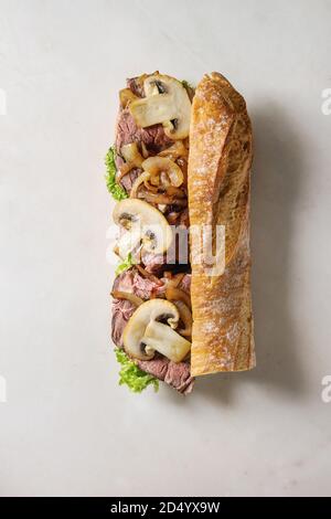 Rindfleisch baguette Sandwich mit Champignon Pilze, grüner Salat, gebratenen Zwiebeln mit Zutaten oben auf weißem Hintergrund. Flach, Raum Stockfoto