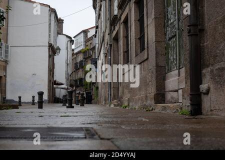 Santiago de Compostela, Galicia, Spanien - 09/26/2020: Öffnung zu einer engen, ruhigen, gepflasterten Straße an einem regnerischen Tag in der Altstadt von Santiago de Compostela. Stockfoto