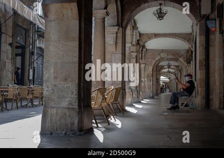 Santiago de Compostela, Galicia, Spanien - 09/22/2020: Älterer spanischer Mann, der unter Steinbögen auf der Straße Gitarre spielt und eine medizinische Maske trägt. Stockfoto