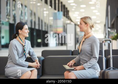 Seitenansicht Porträt von zwei Flugbegleitern, die auf der Couch in der Wartelounge des Flughafens sitzen und einander anblicken, Platz kopieren Stockfoto