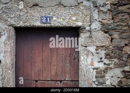 Rustikale rustikale spanische Holztür in einer abgenutzten verwitterten Steinwand mit der Nummer 21 über dem Rahmen gesetzt. Landhaus Bauernhaus rusic uneben. Stockfoto