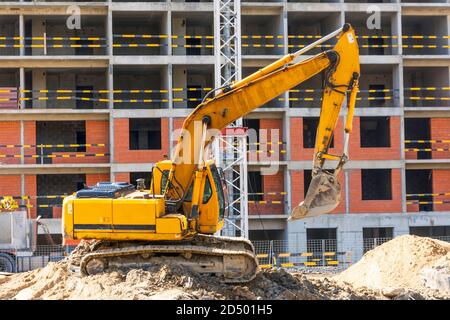 Bagger mit erhöhten Eimern auf dem Hintergrund eines mehrstöckigen Wohngebäudes im Bau Stockfoto