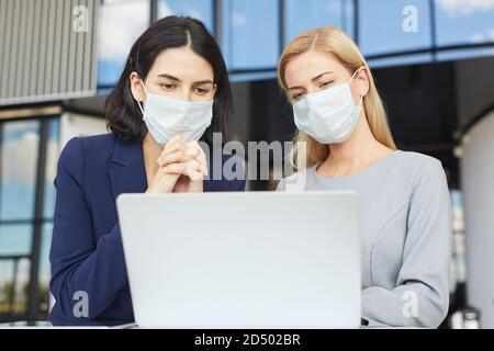 Taille up Porträt von zwei erfolgreichen Geschäftsfrauen tragen Masken während Blick auf den Laptop-Bildschirm, der am Schreibtisch im Bürogebäude steht Stockfoto