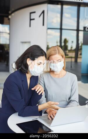 Vertikale Taille nach oben Porträt von zwei erfolgreichen Geschäftsfrauen tragen Masken Während Sie auf den Laptop-Bildschirm schauen, der am Schreibtisch im Büro steht Gebäude Stockfoto