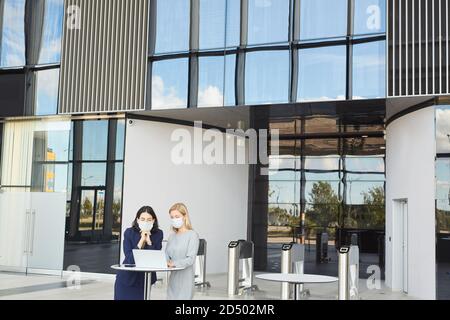 Weitwinkel-Porträt von zwei erfolgreichen Geschäftsfrauen tragen Masken beim Blick auf Laptop-Bildschirm stehen am Schreibtisch im Bürogebäude, Kopierer Platz Stockfoto