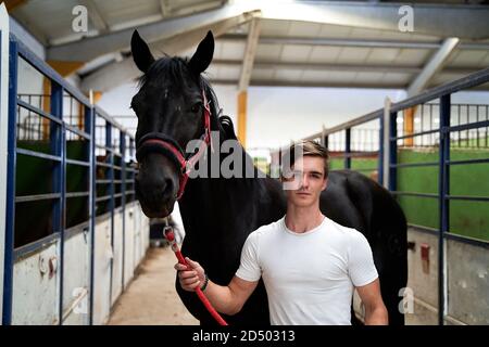 Junge kaukasische Männchen posiert mit seinem Pferd vor einem Reiten Klasse Stockfoto