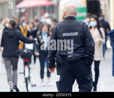 Düsseldorf, Deutschland. Oktober 2020. Ein Angestellter der Ordnungsbehörde sieht Passanten mit und ohne Mund- und Nasenschutz durch eine Einkaufsstraße gehen. In vielen Großstädten in Nordrhein-Westfalen ist die Zahl der neuen Coronainfektionen pro 100,000 Einwohner innerhalb einer Woche über die entscheidende Schwelle von 50 gestiegen. Quelle: Roland Weihrauch/dpa/Alamy Live News Stockfoto