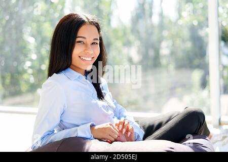 Portrait von lächelnd ziemlich schwarz Business Frau entspannen und posieren in modernen kreativen Büro mit Panoramafenstern.. Pausenzeit Konzept, Geschäft Erfolg Stockfoto