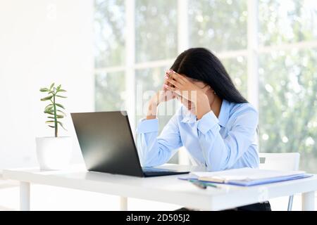 Gestresste müde Geschäftsfrau schloss Gesicht von zwei Händen im modernen Büro sitzen. Problemkonzept Stockfoto