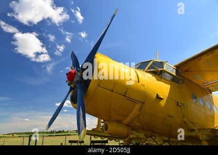 Nahaufnahme einer alten gelben Ebene. Isolierte gelbe Bi-Ebene auf grasbewachsenen Wiese unter blauem Himmel mit dynamischen Wolken. Flugzeug auf einem grasbewachsenen Flugplatz. Stockfoto