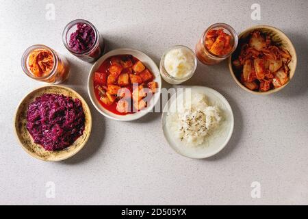 Vielzahl von fermentierter Lebensmittel traditionellen koreanischen Kimchi Kohl und Rettich Salat, Weiß und Rot, Sauerkraut in Glas und keramische Platten über graue Fleck Stockfoto