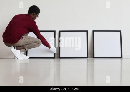 Full length Portrait of African-American man Einrichtung von leeren schwarzen Rahmen auf dem Boden während der Planung einer Kunstgalerie oder Ausstellung, kopieren Raum Stockfoto