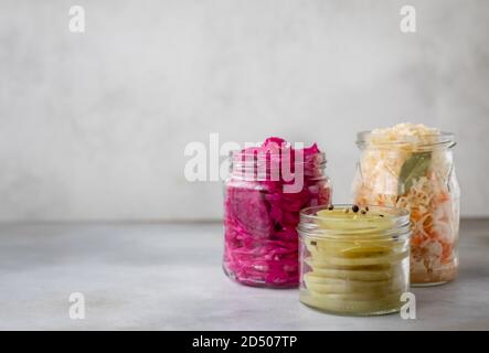 Verschiedene fermentierte Gemüse in Gläsern. Kohl, grüne Tomaten. Grauer Hintergrund, Kopierraum, horizontales Bild Stockfoto