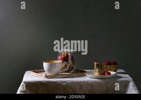 2-in-1-Dessert im Glas. Keks, Kaffeesahne, Muttern, Himbeeren, frischer Minze. Mit Tasse Kaffee Espresso, Beeren und kanne Milch über Grau li serviert. Stockfoto