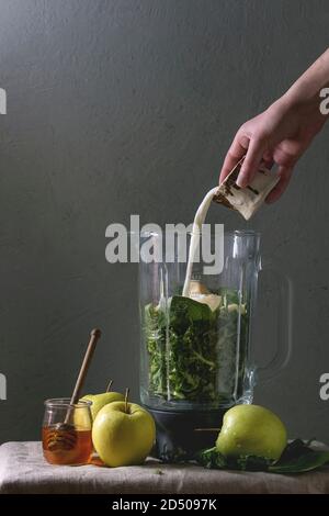 Zutaten für grüne Spinat kale apple Honig Smoothie in Glas Mixer auf Leinen Tischdecke mit Zutaten oben. Junger Mann gießen Milch. Gesund Stockfoto