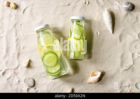 Sommergetränke. Zwei Glasflaschen mit Zitronen- und Gurkenaufguss mit sattem Wasser auf weißem Sand als Hintergrund. Flach liegend, Platz Stockfoto