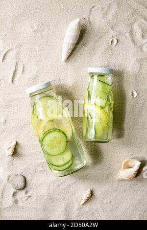 Sommergetränke. Zwei Glasflaschen mit Zitronen- und Gurkenaufguss mit sattem Wasser auf weißem Sand als Hintergrund. Flach liegend, Platz Stockfoto
