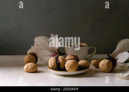 Baci di dama hausgemachte italienische Haselnuss Kekse Kekse mit Schokolade in Keramik Platte mit Tasse Espresso und Magnolia Blumen serviert. Stockfoto