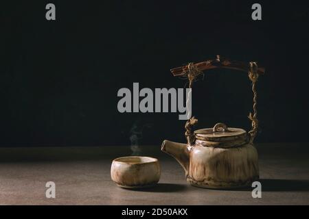 Hot grüner Tee in der traditionellen chinesischen Ton Keramik Tasse und craft handmade Teekanne mit Holzgriff auf dunklen Tisch mit schwarzem Hintergrund. Kopieren Stockfoto