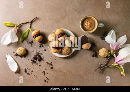 Baci di dama hausgemachte italienische Haselnuss Kekse Kekse mit Schokolade in Keramik Platte mit Tasse Espresso und Magnolia Blumen serviert. Stockfoto