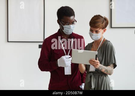Waist-up-Porträt von tätowierten jungen Frau und afroamerikanischen Mann beide mit Masken, während mit digitalen Tablet und Planung Kunstgalerie Ausstellung, Copy Space Stockfoto