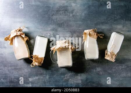 Vielzahl von Nicht-Milchprodukte vegan laktosefrei Nüssen und Getreide, Milch, Mandeln, Haselnuss, Kokos, Reis, Hafer in Glasflaschen in der Zeile über blaue Textur Hintergrund. Stockfoto