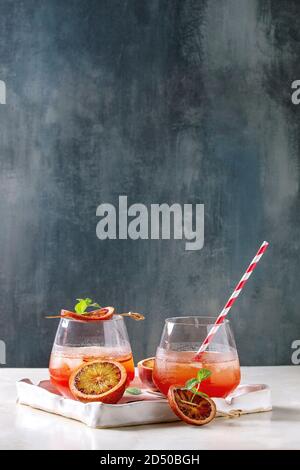 Blutorange Eistee Cocktails in Gläser, durch die Scheibe der Orangen und frischer Minze dekoriert, serviert mit retro Stroh in Keramik Tablett auf weißem Marmor Tabelle wi Stockfoto