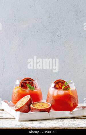 Blutorange Eistee Cocktails in Gläser, durch die Scheibe der Orangen und frischer Minze dekoriert, in Keramik Tablett auf weiße Holztisch serviert mit grauen Wand bei b Stockfoto