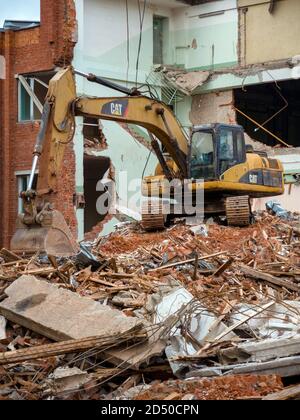 Gelber Bagger auf Abbruchstelle, zerstörte altes Gebäude im Hintergrund Stockfoto
