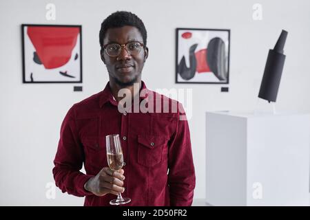 Waist up Portrait von lächelnden afroamerikanischen Mann hält Champagner Glas und Blick auf die Kamera, während posiert in der Kunstgalerie Öffnung, kopieren Raum Stockfoto