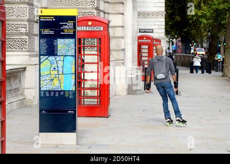 London, England, Großbritannien. Traditionelle rote Telefonzellen in Whitehall - Mann Rollerskaten vorbei Stockfoto