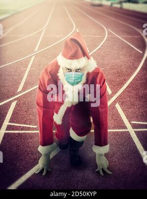 Der Weihnachtsmann in der Startposition auf einer Laufstrecke mit OP-Maske. Stockfoto