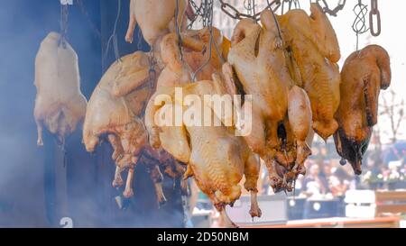 Hängen ganze Hühner rauchen über Feuer oder Kohlen auf Sommer lokalen Lebensmittelmarkt - Nahaufnahme. Kochen im Freien, Grill, Gastronomie, Kochen, Straße Stockfoto