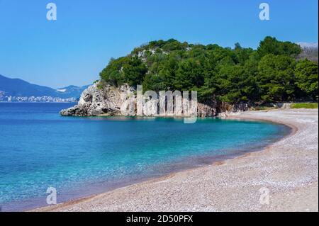Mediterranes blaues Meer, Strand mit kleinen orangefarbenen Kieselsteinen, Felsen mit grünen Pinien.