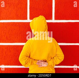 Teenager Mädchen in einem gelben Sweatshirt oder Hoodie in einem Kapuze vor dem Hintergrund einer roten Wand mit weiß Nähte Stockfoto