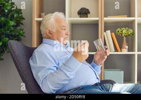 Serious Senior man Einnahme von verordneten Medikamenten sitzen in einem Sessel Im Wohnzimmer Stockfoto