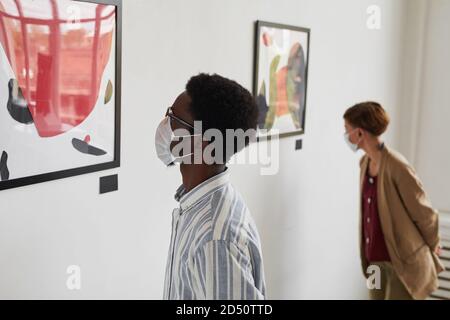 Porträt von zwei jungen Menschen, die Gemälde betrachten, während sie Masken in der Ausstellung moderner Kunst tragen, Kopierraum Stockfoto