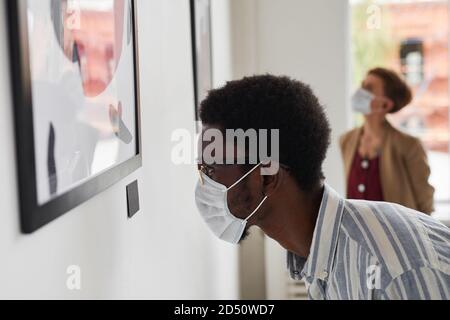 Seitenansicht Porträt eines jungen afroamerikanischen Mannes, der Gemälde ansieht und Maske trägt, in der Ausstellung der modernen Kunstgalerie, Kopierraum Stockfoto