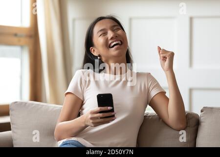 Überglücklich junge asiatische Frau hält Telefon, feiert Erfolg Stockfoto