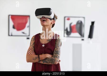 Waist-up-Porträt einer tätowierten jungen Frau, die VR-Ausrüstung trägt, während Sie ein immersives Erlebnis in der Ausstellung der modernen Kunstgalerie „Copy Space“ genießen Stockfoto