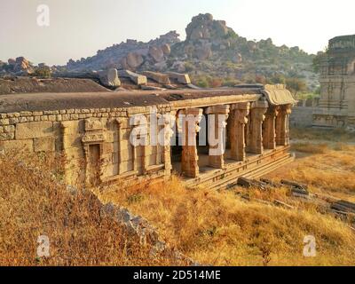 Wand und Säulen von Ruinen in Achyuta Raya Temple Complex bei Sonnenaufgang mit felsigen Hügel im Hintergrund in Hampi, Karnataka, Indien Stockfoto