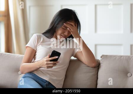 Verärgert junge asiatische Frau weinend, hält Telefon, erhielt schlechte Nachricht Stockfoto