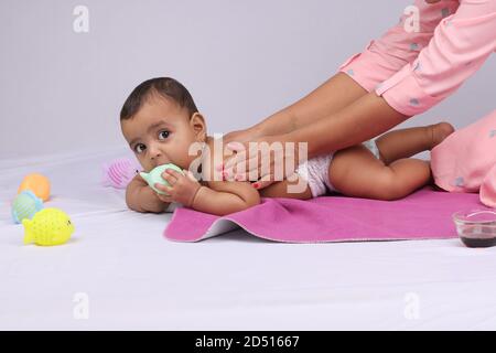 Indische Mutter massiert ihr schönes Baby. Stockfoto