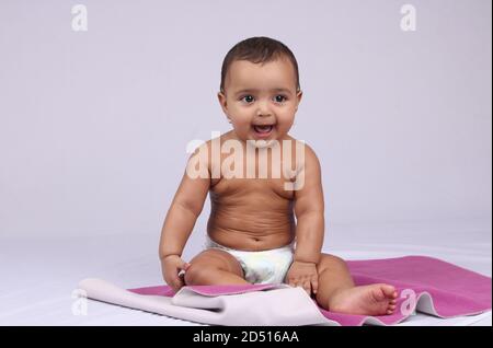 Glücklich aussehendes indisches Baby, das in einer Windel sitzt, nachdem es Öl massiert wurde. Stockfoto