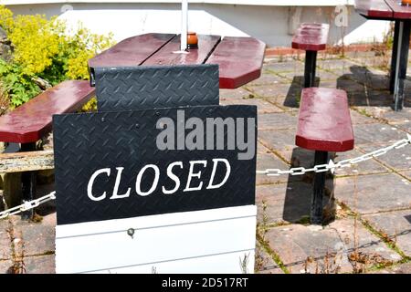 Nahaufnahme des schwarzen und weißen geschlossenen Schildes für das Restaurant Mit leerem rot lackiertem Tisch und Bank im Hintergrund draußen Im Sommer Stockfoto