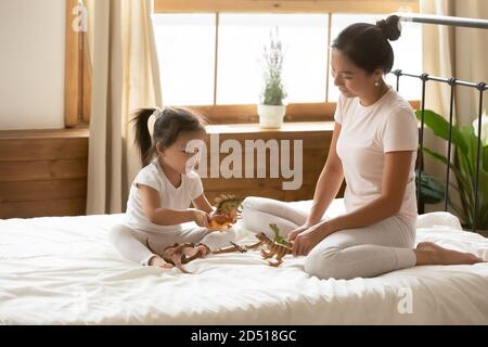 Fürsorgliche junge asiatische Mutter und kleine Tochter spielen Spielzeug Dinosaurier Stockfoto